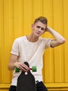 Beautiful teen with a skateboard. Attractive young guy holding a skateboard on a yellow wall background. Youth concept. Royalty Free Stock Photo