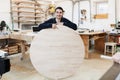 Portrait of a carpenter standing in his woodwork studio carpenter workshop. The man holds a wooden round board for the text.