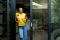 Portrait of casual relaxed woman using phone for online payment on doorstep of her home shopping online from home leaning on door