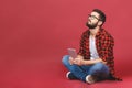 Portrait of casual young man sitting on the floor with his legs crossed and holding a tablet isolated against red background Royalty Free Stock Photo