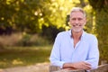 Portrait Of Casually Dressed Mature Man Leaning On Fence On Walk In Countryside