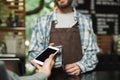 Portrait of caucasian barista man holding consumer terminal for paypass payment while working in street cafe or coffeehouse