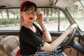 Portrait of Caucasian beautiful young girl in black vintage dress and vintage glasses posing behind the wheel of a vintage car Royalty Free Stock Photo