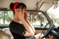 Portrait of Caucasian beautiful young girl in black vintage dress and vintage glasses posing behind the wheel of a vintage car Royalty Free Stock Photo