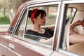 Portrait of a Caucasian beautiful young girl in a black vintage dress, posing in the cabin of a vintage car Royalty Free Stock Photo