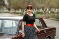 Portrait of a Caucasian beautiful young girl in a black vintage dress, posing near a vintage car Royalty Free Stock Photo