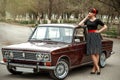 Portrait of a Caucasian beautiful young girl in a black vintage dress, posing near a vintage car Royalty Free Stock Photo