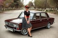 Portrait of a Caucasian beautiful young girl in a black vintage dress, posing near a vintage car Royalty Free Stock Photo