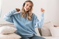 Portrait of caucasian blond girl 20s wearing headphones smiling and listening to music at home Royalty Free Stock Photo