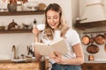 Portrait of caucasian blond woman reading book and drinking tea while standing in stylish wooden kitchen at home Royalty Free Stock Photo