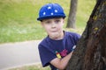 Portrait of a Caucasian boy in a cap peeking from behind a tree. Royalty Free Stock Photo