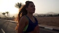 Portrait of caucasian brunette girl jogging at tropical highway at sunrise.