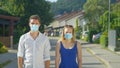 PORTRAIT: Caucasian couple wearing surgical facemasks stand in middle of street