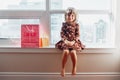 Girl child sitting on window sill at home opening birthday gifts