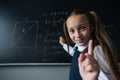 Portrait of a caucasian girl in the classroom. The schoolgirl writes the formula with chalk on the blackboard and looks