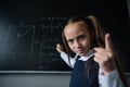 Portrait of a caucasian girl in the classroom. The schoolgirl writes the formula with chalk on the blackboard and looks