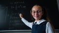 Portrait of a caucasian girl in glasses in the classroom. The schoolgirl writes the formula with chalk on the blackboard Royalty Free Stock Photo