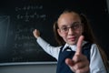Portrait of a caucasian girl in glasses in the classroom. The schoolgirl writes the formula with chalk on the blackboard Royalty Free Stock Photo