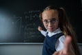 Portrait of a caucasian girl in glasses in the classroom. The schoolgirl writes the formula with chalk on the blackboard