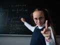 Portrait of a caucasian girl in glasses in the classroom. The schoolgirl writes the formula with chalk on the blackboard