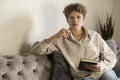 Girl holding glasses in the hand is sitting on the couch and reading a book Royalty Free Stock Photo