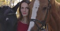 Portrait of a Caucasian girl with problem skin standing with two horses outdoors. Sick woman undergoing hippotherapy in