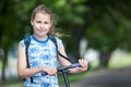 Portrait of Caucasian girl with wheel of kick scooter in hands, outdoors, copy space