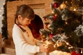Portrait of Caucasian little girl standing near Christmas tree and present boxes, dressed white sweater, having dark hair and Royalty Free Stock Photo