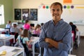 Male school teacher standing with arms crossed in an elementary school classroom Royalty Free Stock Photo