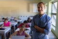 Male school teacher standing with arms crossed in an elementary school classroom Royalty Free Stock Photo