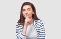 Portrait of Caucasian pretty young woman wears striped shirt, holding index finger on lips, asking to keep silence. Beautiful Royalty Free Stock Photo