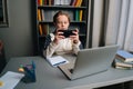 Portrait of Caucasian pupil boy playing video game on mobile phone sitting at desk on online lesson with laptop Royalty Free Stock Photo