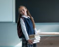Portrait of a caucasian schoolgirl with a backpack. The girl is holding a stack of textbooks in the classroom.