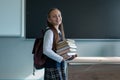 Portrait of a caucasian schoolgirl with a backpack. The girl is holding a stack of textbooks in the classroom.