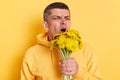 Portrait of Caucasian sick ill man wearing casual style hoodie posing isolated over yellow background, holding bouquet of Royalty Free Stock Photo