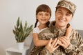 Portrait of Caucasian smiling mother and her child, woman wearing camouflage uniform and cap posing with her daughter, looking at Royalty Free Stock Photo