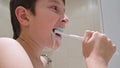 A portrait of a caucasian teen boy brushing teeth in bathroom, close up