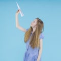 Portrait of Caucasian Teenage Girl in Blue Checked Dress Launching Origami Paper Plane Posing Over Blue Background Royalty Free Stock Photo