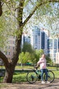 Portrait of Caucasian teenage girl standing with her bicycle under tree in urban park Royalty Free Stock Photo