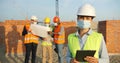 Portrait of Caucasian woman constructor in casque and medical mask standing outdoors at construction. Female builder or