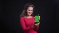 Portrait of caucasian woman in red smilingly showing green screen of tablet into camera on black background.