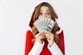 Portrait of caucasian woman 20s wearing Santa Claus red costume smiling and holding fan of money in dollar banknotes, isolated Royalty Free Stock Photo