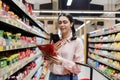 Portrait of Caucasian woman scan qr code of product using smartphone. Shelves with food in background. Concept of