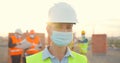 Portrait Caucasian young female constructor in casque and medical mask standing outdoor at construction. Close up of