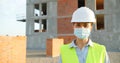 Portrait of Caucasian young pretty woman constructor in casque and medical mask standing outdoor at construction and