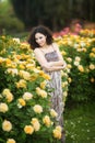 A portrait of Caucasian young woman near yellow roses bush in a rose garden, looking straight to the camera Royalty Free Stock Photo