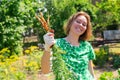 Portrait of caucasian young woman with a smile holds a bunch of carrots collected from the garden.Vegetation in the background.