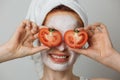 Portrait of caucasian young woman with white cosmetic mask on face and slices of tomato on eyes