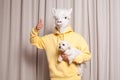 Portrait of ceative lama person in yellow hoodie holding little white dog showing thumb up on beige studio wall background