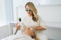 Portrait of certified cosmetologist wearing protective glasses conducting facial rejuvenation using modern apparatus for